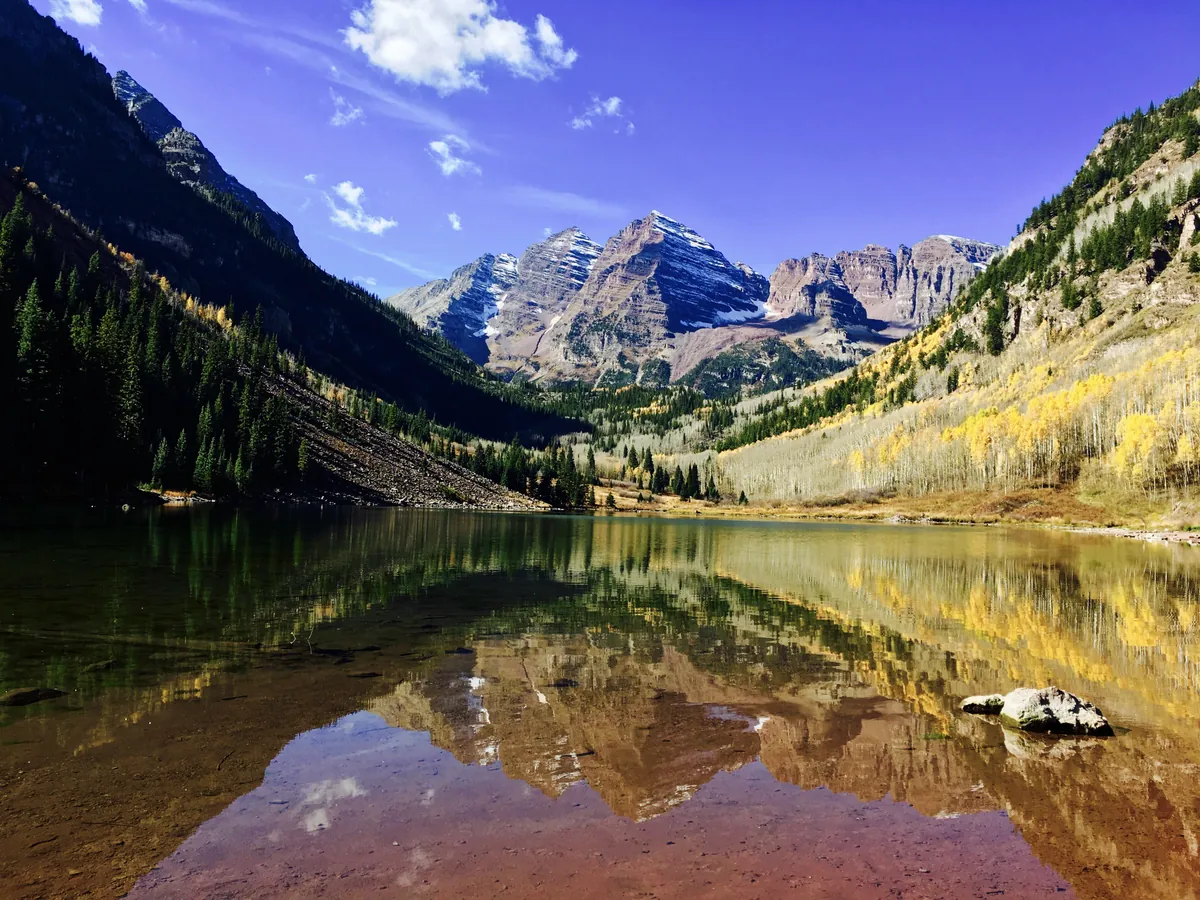 Golden aspens on the slopes above Maroon Lake in Colorado's Maroon Bells valley, with the peaks reflected in the water