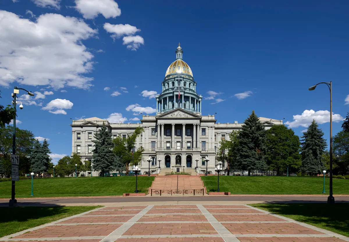 The Colorado State Capitol in Denver, with its gold dome, under a blue sky with scattered clouds.