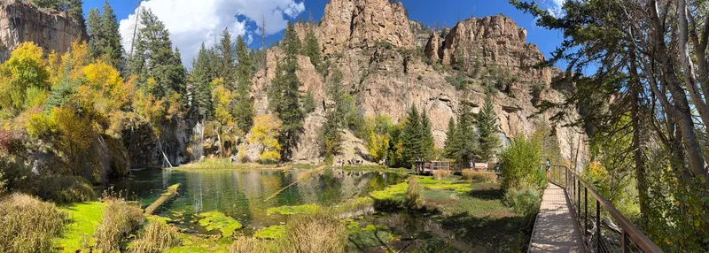 Panorama from the railed boardwalk at Hanging Lake, looking across the lake to towering canyon cliffs.