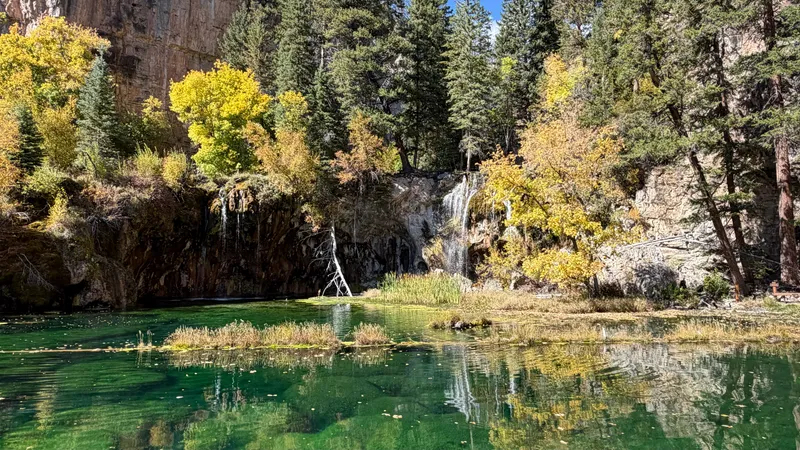 Hanging Lake's emerald water and travertine shelf below Bridal Veil Falls, framed by golden fall aspens and spruce