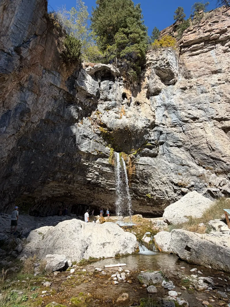 Spouting Rock, where a twin ribbon of water pours from an opening partway up a gray limestone cliff above a pool.
