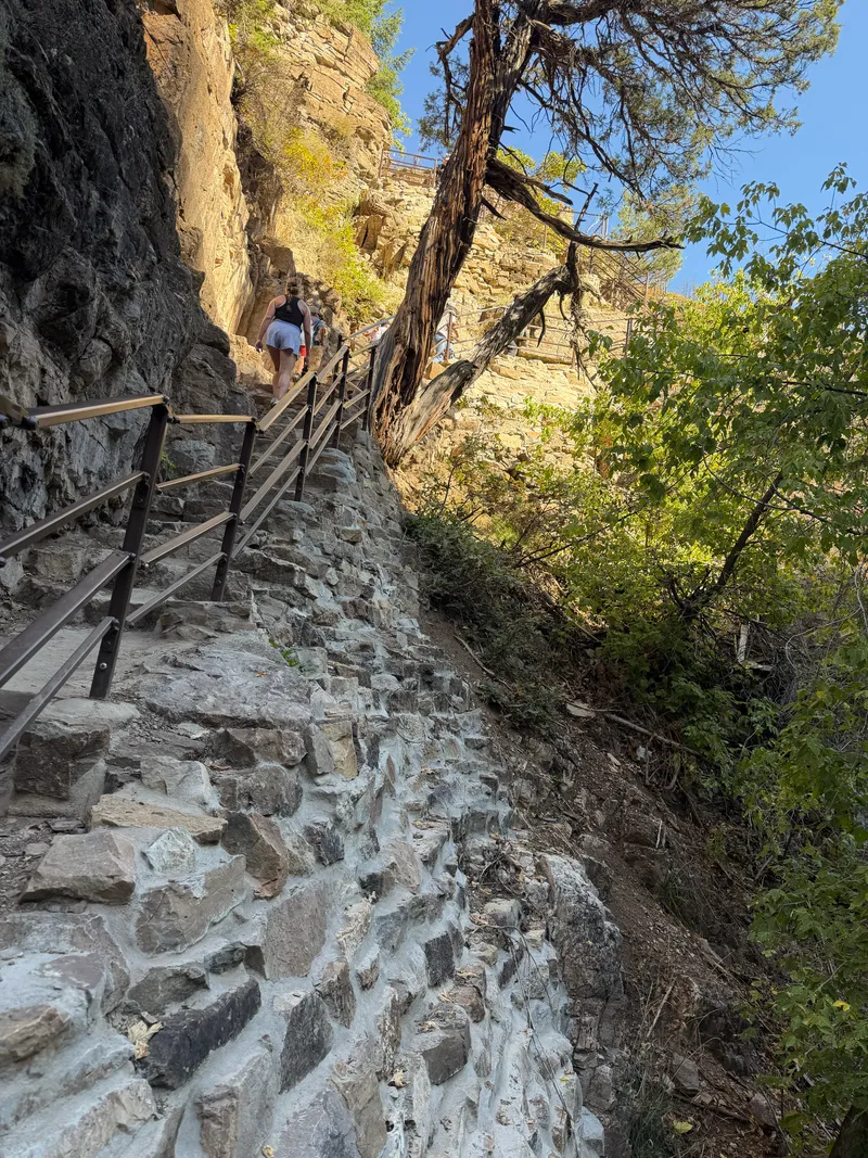 Steep staircase of mortared stone steps with metal railings climbing a cliff below the lake.