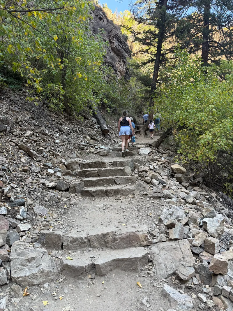 Hikers climbing rough-cut stone steps on the Hanging Lake Trail through a rocky slope.